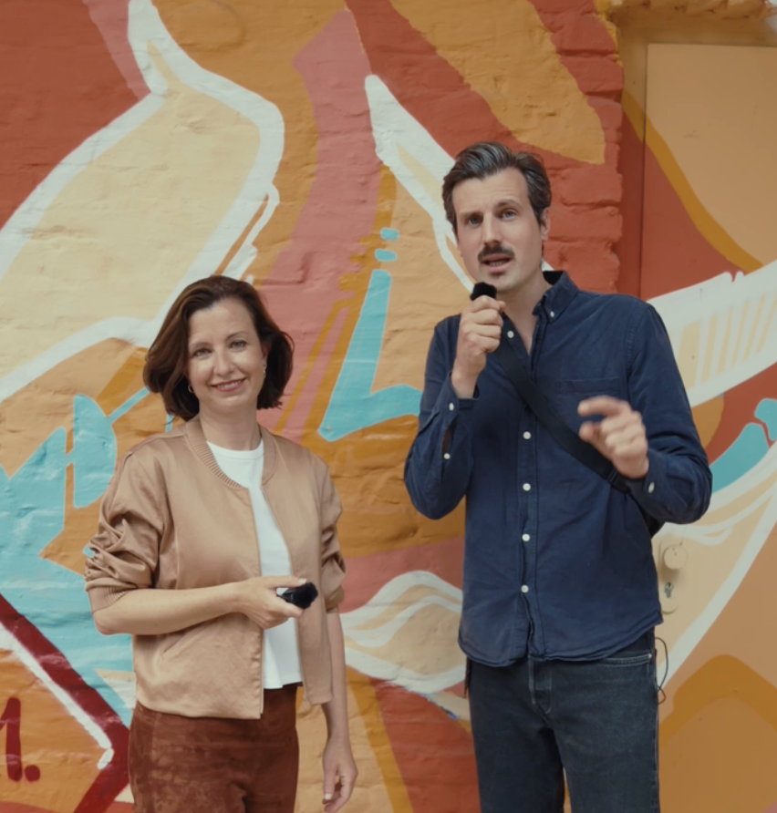 Zwei Volt Berlin Kandidierende sprechen vor einer bunten Berliner Wandmalerei